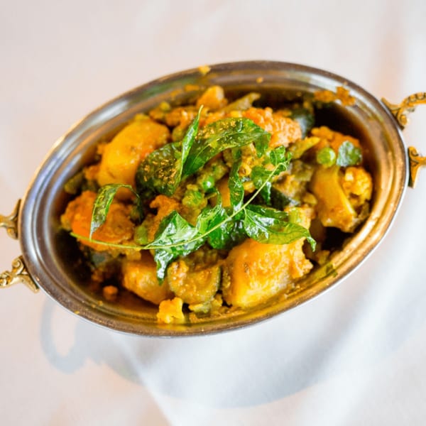Maharaja Indian Restaurant's mixed vegetable curry, garnished with fresh green herbs in a silver bowl.
