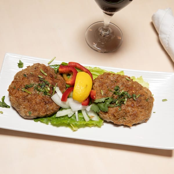 Two Maharaja Indian Restaurant kebabs on lettuce with lemon, red peppers, and onions, next to a wine glass.