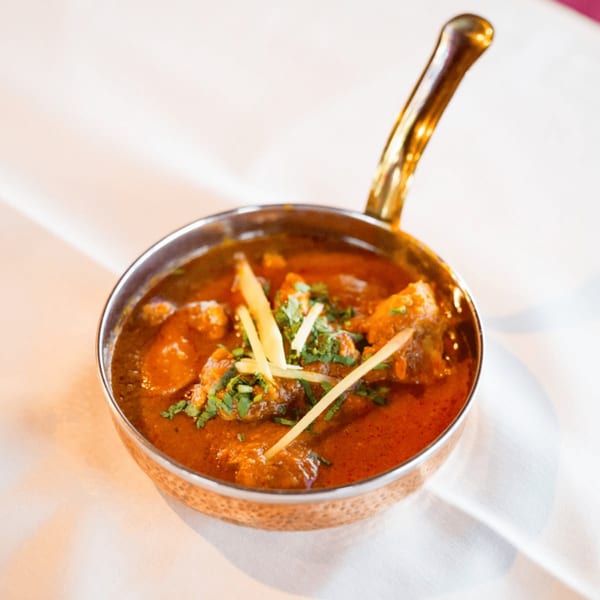 Maharaja Indian Restaurant's chicken curry, garnished with ginger and cilantro, in a copper serving dish.
