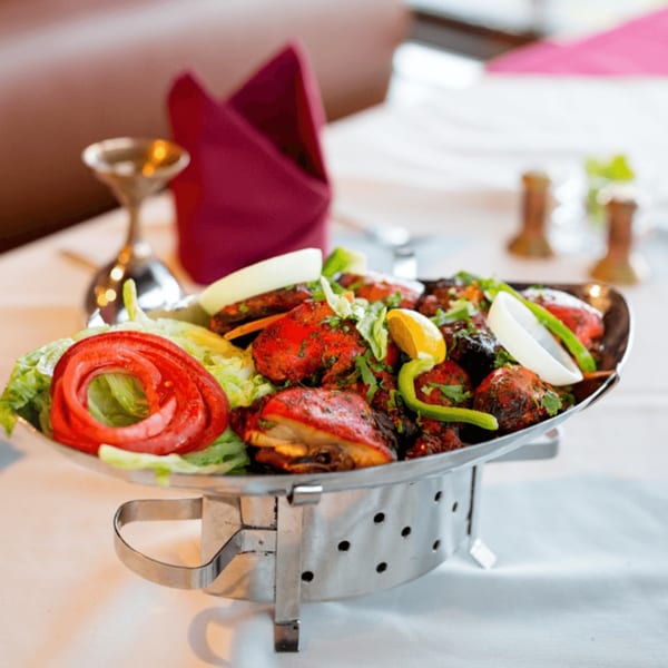 Maharaja Indian Restaurant's Tandoori chicken, garnished with fresh vegetables, served on a metal platter.
