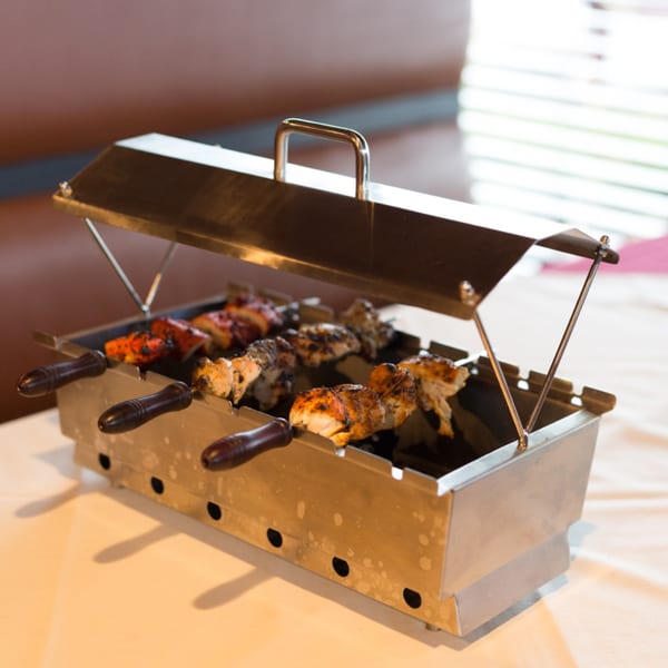 A metal tandoor grill with skewers of chicken tikka and other Indian meats on a white tablecloth.