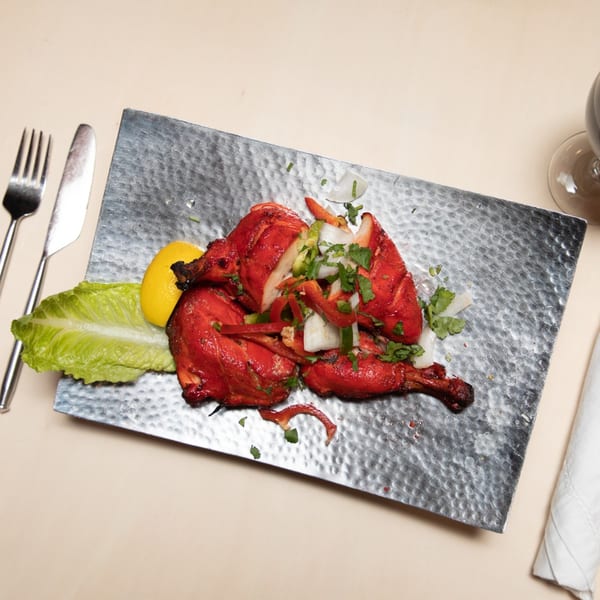 Maharaja Indian Restaurant's Tandoori Chicken, garnished with lemon, lettuce, onions, and peppers on a metal plate.