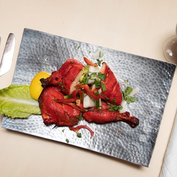Maharaja Indian Restaurant's Tandoori Chicken, garnished with onions, peppers, cilantro, and lemon on a hammered metal plate.