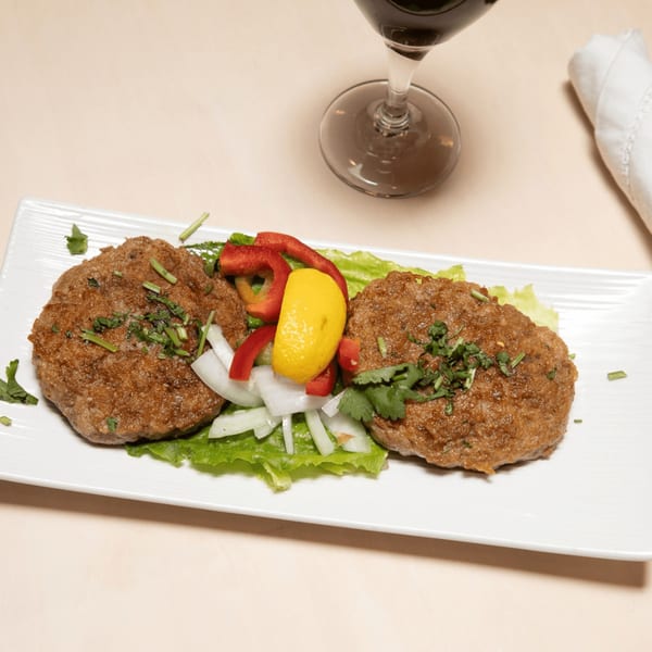 Two Indian Maharaja patties on lettuce with red peppers, onions, lemon, and cilantro.