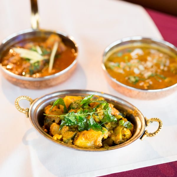 Three copper bowls of Indian curries and stews, one garnished with fresh green herbs.