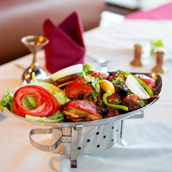 Maharaja Indian Restaurant's Tandoori Chicken, garnished with fresh vegetables, on a silver serving dish.